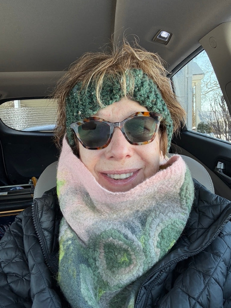 Person wearing a green knitted headband and sunglasses inside a car.